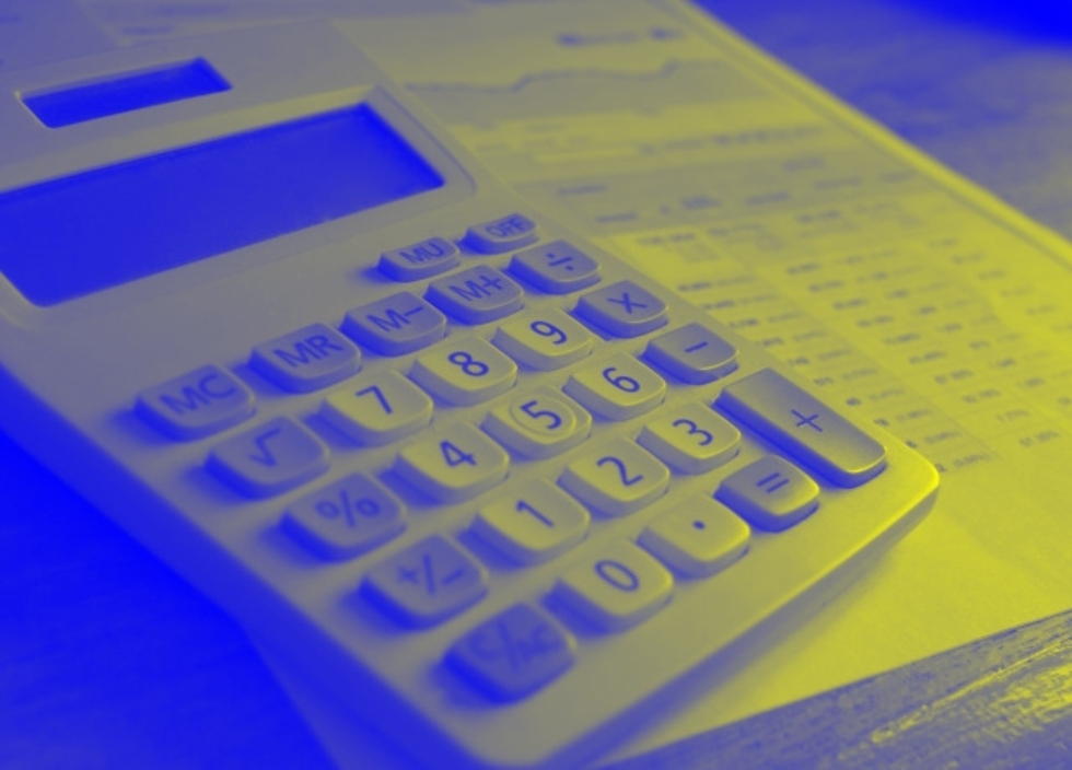Yellow-and-blue-tinted monochrome photo showing a basic electronic calculator with a printed page of financial information on a desk Yellow-and-blue-tinted monochrome photo showing a basic electronic calculator with a printed page of financial information on a desk